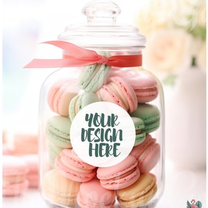Può includere: Un barattolo di vetro pieno di macarons rosa pastello e verdi. Un adesivo circolare bianco con il testo "YOUR DESIGN HERE" è sul davanti del barattolo.