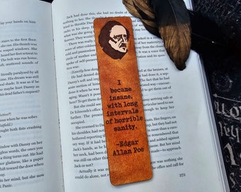 Puede incluir: Un marcapáginas de madera marrón con una cita de Edgar Allan Poe: "Me volví loco, con largos intervalos de horrible cordura." El marcapáginas también presenta un retrato de Edgar Allan Poe.