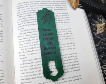 以下が含まれることがあります： 雷のデザインと「Beware: For I am fearless and therefore powerful.」というテキストが書かれた緑色の革製しおり。しおりには人の頭の切り抜きデザインが施されています。