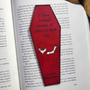 May include: A red wooden coffin-shaped bookmark with a quote from Dracula by Bram Stoker. The quote reads "I have crossed oceans of time to find you." Two bats are cut out of the bookmark.