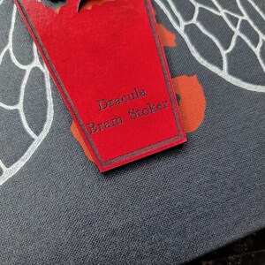 May include: A red book cover with a white insect design and a red coffin-shaped bookmark with the text "Dracula Bram Stoker" in black.