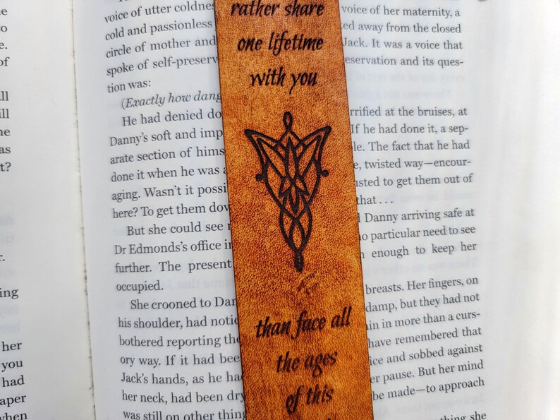 May include: A brown leather bookmark with a black design of the One Ring from the Lord of the Rings. The bookmark has the quote "Rather share one lifetime with you than face all the ages of this" inscribed on it.