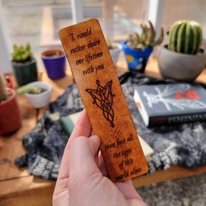 May include: A brown leather bookmark with a quote from the Lord of the Rings: "I would rather share one lifetime with you than face all the ages of this world alone." The bookmark features a design of the One Ring.