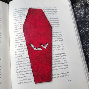 May include: A red coffin-shaped bookmark with two bats cut out of the front. The bats have the word "ewwwinder" written on them.