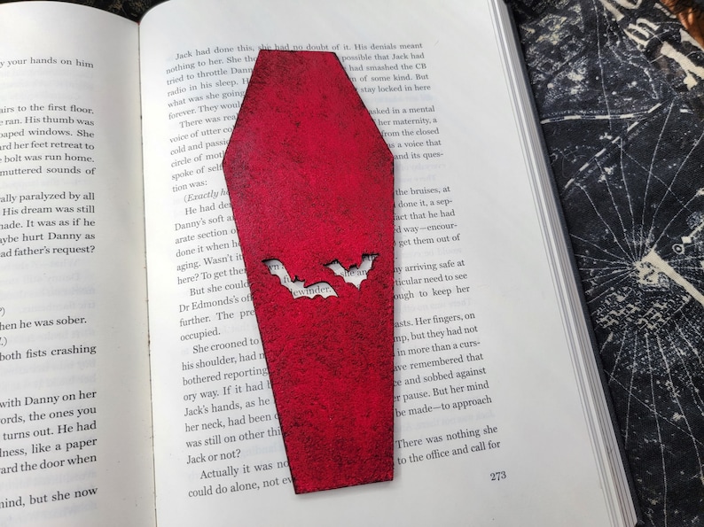 May include: A red coffin-shaped bookmark with two bats cut out of the front. The bats have the word "ewwwinder" written on them.