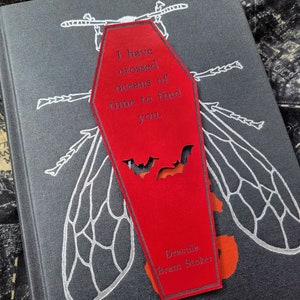 May include: Red coffin-shaped bookmark with a white bat silhouette and the text "I have crossed oceans of time to find you." and "Dracula Bram Stoker" printed on the front.