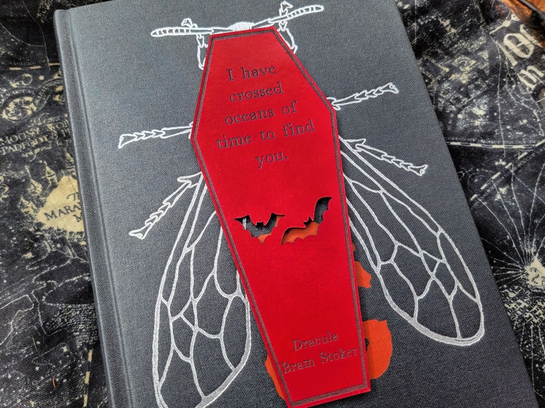 May include: Red coffin-shaped bookmark with a white bat silhouette and the text "I have crossed oceans of time to find you." and "Dracula Bram Stoker" printed on the front.