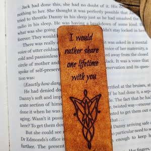 May include: A brown leather bookmark with a wood-burned design of the One Ring from The Lord of the Rings. The bookmark has the text "I would rather share one lifetime with you" inscribed on it.