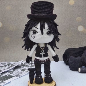 May include: Crocheted doll with black hair, wearing a black top hat, black and white outfit, and holding a black umbrella. The doll is standing on a wooden base.