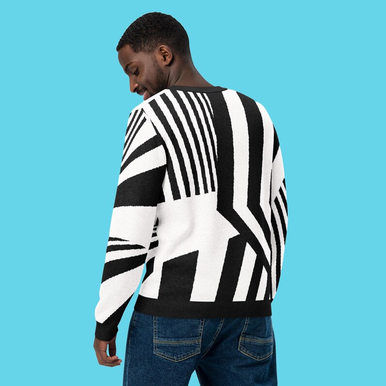 K&ouml;nnte beinhalten: Ein schwarz-wei&szlig; gemusterter Pullover. Der Pullover hat ein auff&auml;lliges Design mit vertikalen und abgewinkelten Streifen und Formen. Die Person tr&auml;gt eine blaue Jeans. Der Hintergrund ist einfarbig hellblau.