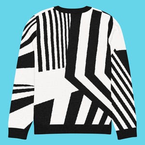 K&ouml;nnte beinhalten: Schwarz-wei&szlig; gemusterter Pullover. Der Pullover hat ein auff&auml;lliges geometrisches Design mit dicken schwarzen Streifen und eckigen Formen auf wei&szlig;em Hintergrund. Der lang&auml;rmlige Pullover hat einen Rundhalsausschnitt und gerippte B&uuml;ndchen.