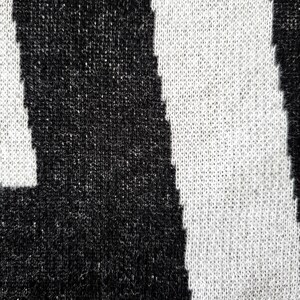 K&ouml;nnte beinhalten: Nahaufnahme eines Strickstoffs mit einem auff&auml;lligen schwarz-wei&szlig; gestreiften Muster. Die Textur des Stricks ist sichtbar, mit einer Mischung aus schwarzen und wei&szlig;en F&auml;den, die das Design bilden. Die Streifen sind vertikal und gleichm&auml;&szlig;ig angeordnet.