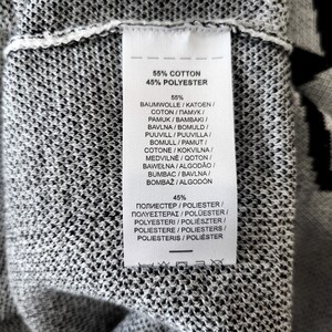 K&ouml;nnte beinhalten: Nahaufnahme eines wei&szlig;en Stoffetiketts mit schwarzem Text. Das Etikett gibt die Materialzusammensetzung an: 55 % Baumwolle und 45 % Polyester. Zus&auml;tzlicher Text listet die Materialnamen in mehreren Sprachen auf.