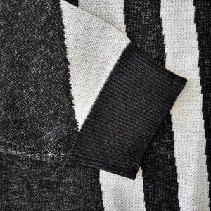 K&ouml;nnte beinhalten: Nahaufnahme eines schwarz-wei&szlig; gestreiften Pullovers. Der &Auml;rmel ist sichtbar, mit einer schwarzen Manschette und einem wei&szlig;-schwarzen Muster. Der Stoff scheint gestrickt zu sein.
