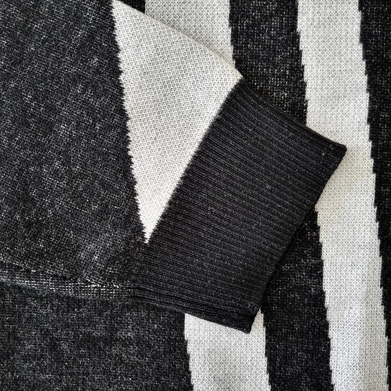 K&ouml;nnte beinhalten: Nahaufnahme eines schwarz-wei&szlig; gestreiften Pullovers. Der &Auml;rmel ist sichtbar, mit einer schwarzen Manschette und einem wei&szlig;-schwarzen Muster. Der Stoff scheint gestrickt zu sein.