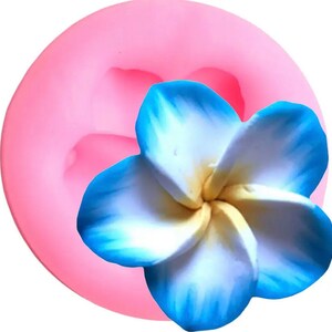 May include: Pink silicone mold for making a blue and yellow plumeria flower. The mold is shaped like a flower with five petals.