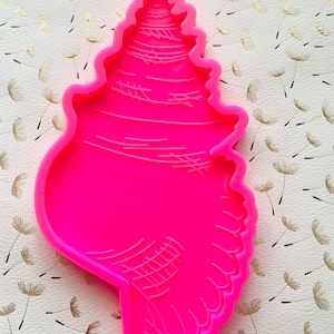 May include: A bright pink silicone mold shaped like a seashell. The mold has a detailed design of a seashell with ridges and lines.