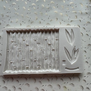 May include: White silicone mold with two designs: a bamboo pattern and a single leaf. The mold is used for creating decorative elements for cakes or other desserts.