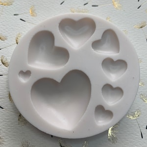 May include: A white silicone mold with seven heart-shaped cavities of varying sizes. The mold is designed for making chocolate, candy, or other treats.