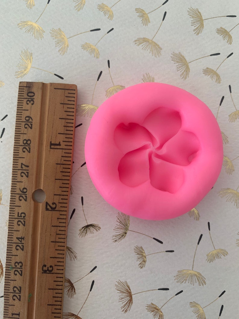 May include: Pink silicone mold with a five-petal flower design. The mold is approximately 2 inches in diameter.