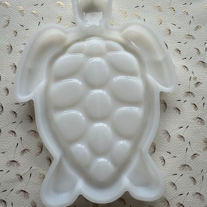 May include: White ceramic turtle shaped dish. The dish has a smooth, glossy finish and is designed to resemble a turtle with a shell and four legs.