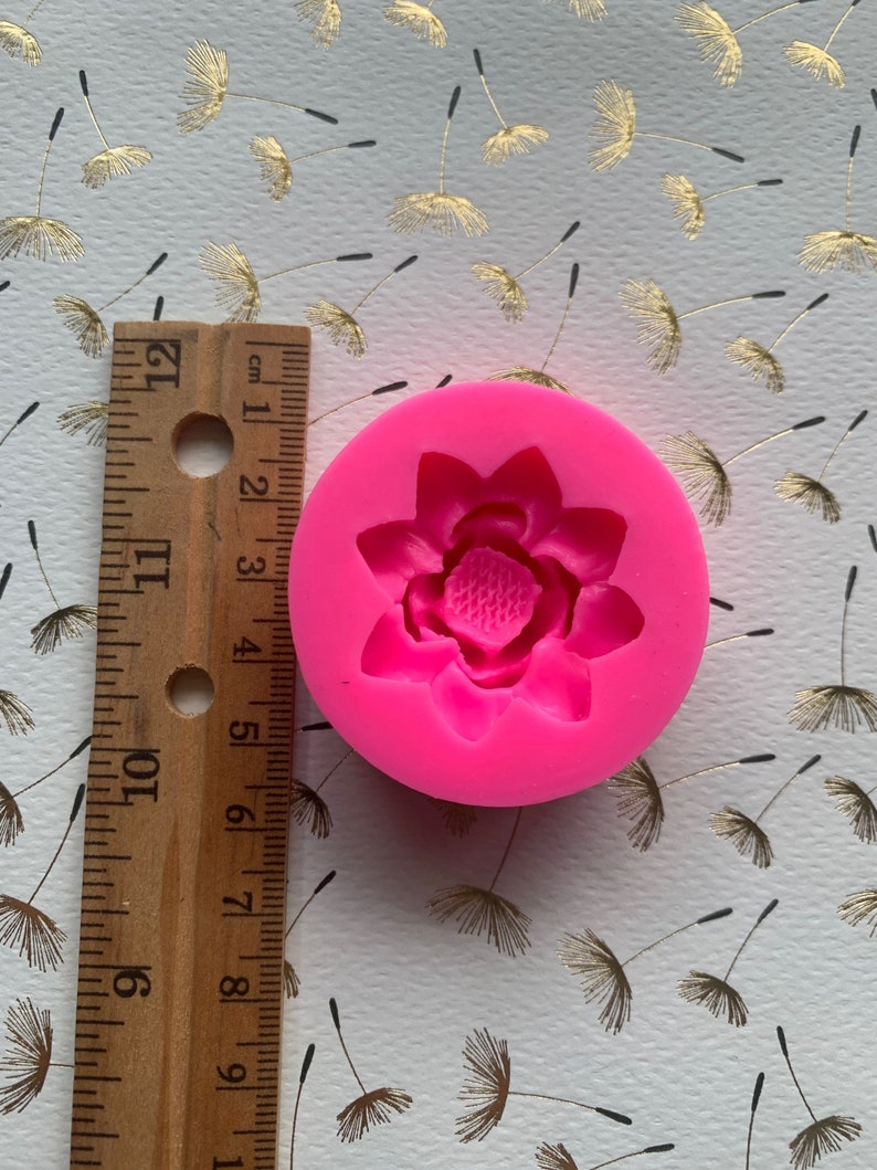 May include: Pink silicone mold with a single cavity shaped like a flower. The flower has five petals and a center with a raised design.