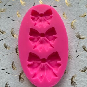 May include: Pink silicone mold with three bow shapes. The mold is designed to create fondant or gum paste bows for cake decorating.
