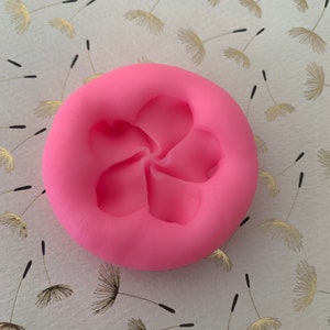 May include: Pink silicone mold with a five-petal flower design. The mold is round and has a smooth surface.