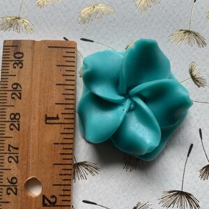 May include: A teal blue resin flower with five petals. The flower is approximately 2 inches in diameter.