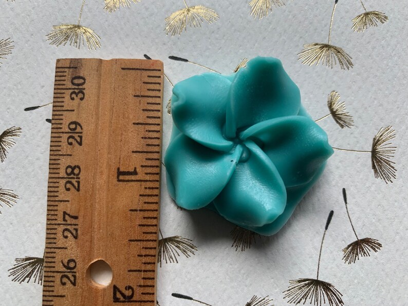 May include: A teal blue resin flower with five petals. The flower is approximately 2 inches in diameter.