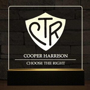 May include: Illuminated sign with a black base and a gold trim. The sign features a white shield with the letters CTR in black. Below the shield, the text reads "COOPER HARRISON" and "CHOOSE THE RIGHT" in white.