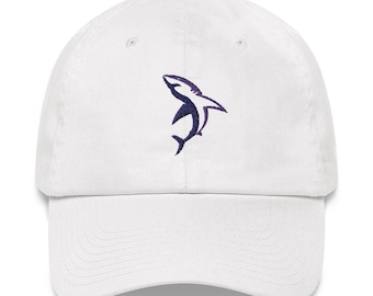 May include: White baseball cap with a curved brim. The cap features a navy blue and purple embroidered shark design on the front. The cap is made of a soft, durable fabric and has an adjustable strap for a comfortable fit.
