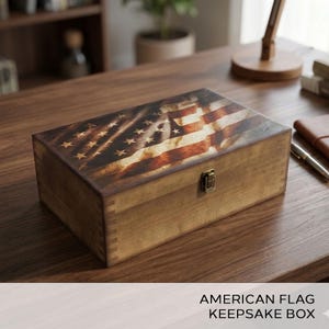 May include: Wooden keepsake box with a distressed American flag design on the lid. The box is rectangular with a brass-colored clasp. The text "AMERICAN FLAG KEEPSAKE BOX" is at the bottom.