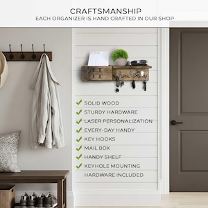 Pu&ograve; includere: Un organizer da parete in legno con ganci per chiavi, una fessura per la posta e un piccolo ripiano. L'organizer &egrave; montato su una parete bianca e presenta il testo "Craftsmanship" e "Each organizer is hand crafted in our shop."