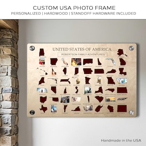 Op de afbeelding: Een houten fotolijst van de VS met de tekst "CUSTOM USA PHOTO FRAME" en "UNITED STATES OF AMERICA". De lijst heeft staatscontouren met foto-inzetstukken en afstandshouders. De tekst "Handmade in the USA" is ook zichtbaar.