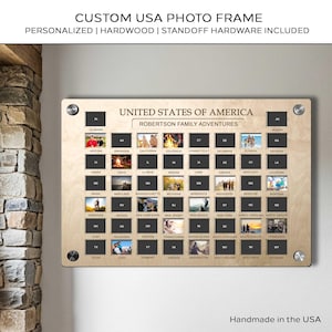 Op de afbeelding: Een aangepaste USA-fotolijst van hardhout. De lijst toont een kaart van de Verenigde Staten met ruimtes voor foto's die elke staat vertegenwoordigen. De tekst "United States of America" en "Robertson Family Adventures" worden weergegeven. De lijst bevat afstandshouders.