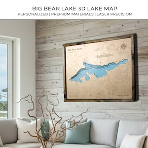 Può includere: Una mappa 3D incorniciata del lago Big Bear, in California, con la scritta "Harrisons" e una rosa dei venti. La mappa presenta acqua blu e uno sfondo in legno marrone chiaro, con la scritta "BIG BEAR LAKE 3D LAKE MAP".