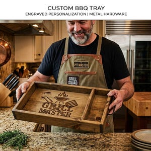 May include: A rectangular wooden serving tray with dark metal handles on the sides. The tray features a laser-engraved design of a grill, a spatula, and a pair of tongs above the text "GRILL MASTER". The tray has a divider on the right side.