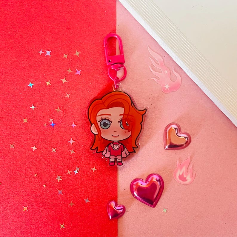 May include: A pink and red cartoon character keychain with a red heart, a pink heart, and a pink flame design. The keychain is made of clear acrylic and has a shiny finish.