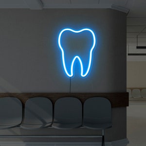 Puede incluir: Una sala de espera en un consultorio dental con un letrero de diente de neón azul en la pared y una fila de sillas grises.