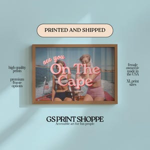 May include: Framed print with a vintage-style image of two people on a boat, with the text "see you On The Cape" in pink. The frame is a light brown color. The print is on a light blue background. The text "high quality prints" and "premium frame options" are on the left.