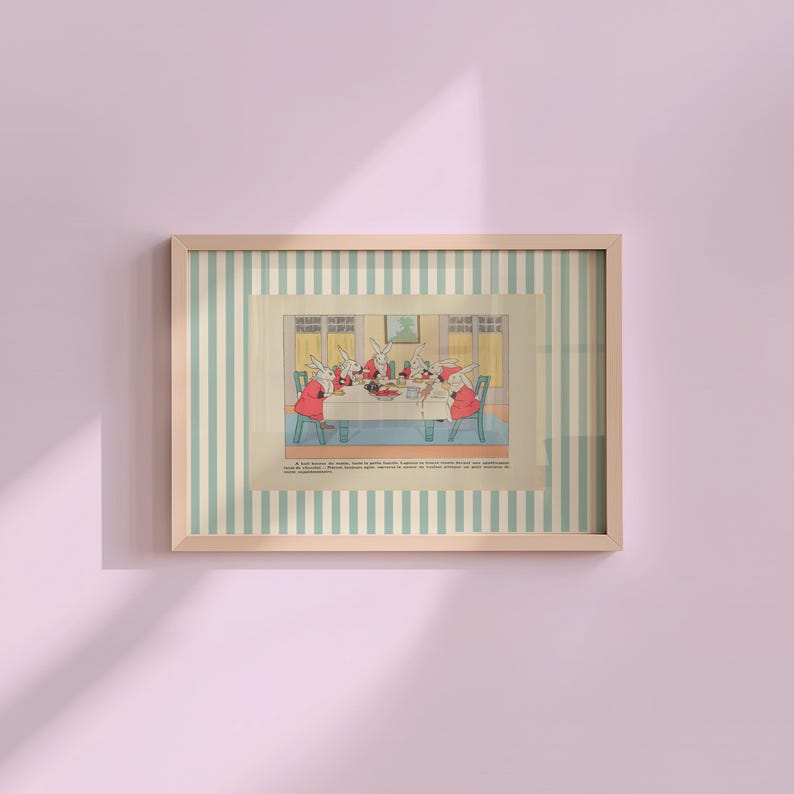 May include: A framed vintage illustration depicts rabbits gathered around a table, dressed in red coats. The artwork is set against a striped background of light blue and white, encased in a wooden frame. The image is mounted on a pink wall.