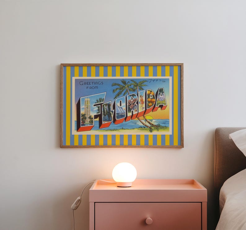 K&ouml;nnte beinhalten: Gerahmte Vintage-Postkartenkunst mit dem Wort "FLORIDA" in gro&szlig;en, farbenfrohen Buchstaben. Das Kunstwerk zeigt einen blauen Himmel, Palmen und einen Sonnenuntergang. Der Rahmen hat einen gelb-blauen Streifen.