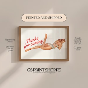 May include: A framed print featuring a vintage pin-up illustration. The artwork depicts a woman in a swimsuit with the text "Thanks for coming" in red script. The print is in a brown frame, with text indicating high-quality prints and XL print sizes.