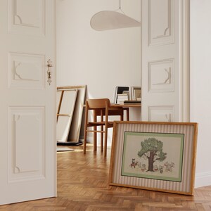 May include: A framed illustration featuring a tree with cartoon characters, set against a green and white striped background. The artwork is in a light brown wooden frame, resting on a wooden floor. The scene is viewed through an open doorway.
