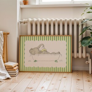 May include: A framed print featuring a cartoon elephant taking a bath in a tub. The artwork has a light green and cream color scheme, with a striped border. The elephant is gray, and the tub has green feet.