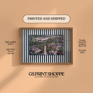 May include: Framed print featuring a detailed aerial view of a university campus, set against a backdrop of navy blue and white vertical stripes. The print is encased in a light brown frame. The text "PRINTED AND SHIPPED" is visible.