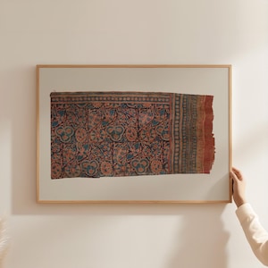 Puede incluir: Textil enmarcado con un detallado diseño floral en tonos rojos, azules y marrones. La tela, con un borde deshilachado, se presenta en un marco de madera.