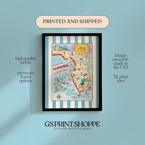 May include: Framed vintage-style map of Florida with a black frame. The map features illustrations of landmarks and wildlife, with the text "Greetings From Florida". The print is on a blue and white striped background. The text "GS PRINT SHOPPE" is at the bottom.