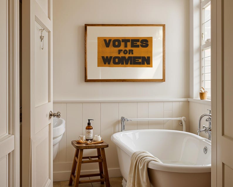 gs print shoppe, gsprintshoppe.com, vintage-style suffrage poster art print featuring bold black text 'VOTES FOR WOMEN' on an orange-yellow banner, framed in minimalist wood and displayed in bright modern interiors